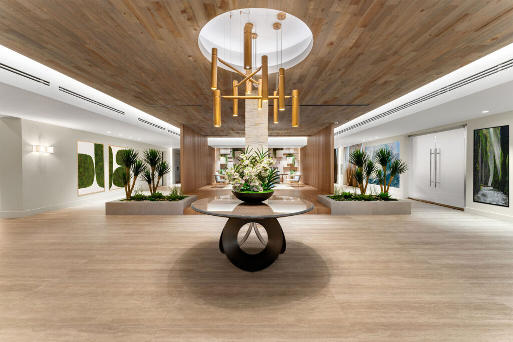 Modern and elegant lobby of The Roney Palace with natural elements and contemporary design details. Modern lobby of The Roney Palace with gold pendant lighting, wooden ceiling, decorative plants, and a central table with a floral arrangement.